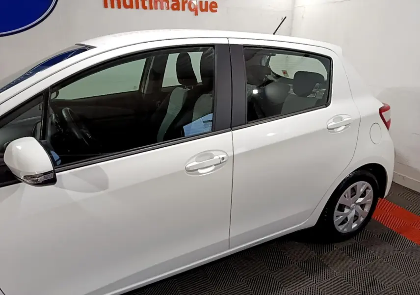 Profil côté gauche d'une Toyota Yaris blanche 2020 hybride, avec rétroviseur blanc et poignées de porte assorties.
