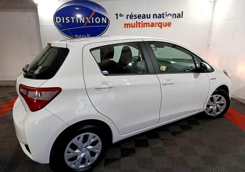 Vue côté droit d'une Toyota Yaris blanche 1.5 Hybride 2020 en intérieur avec jantes alliage et vitres teintées.