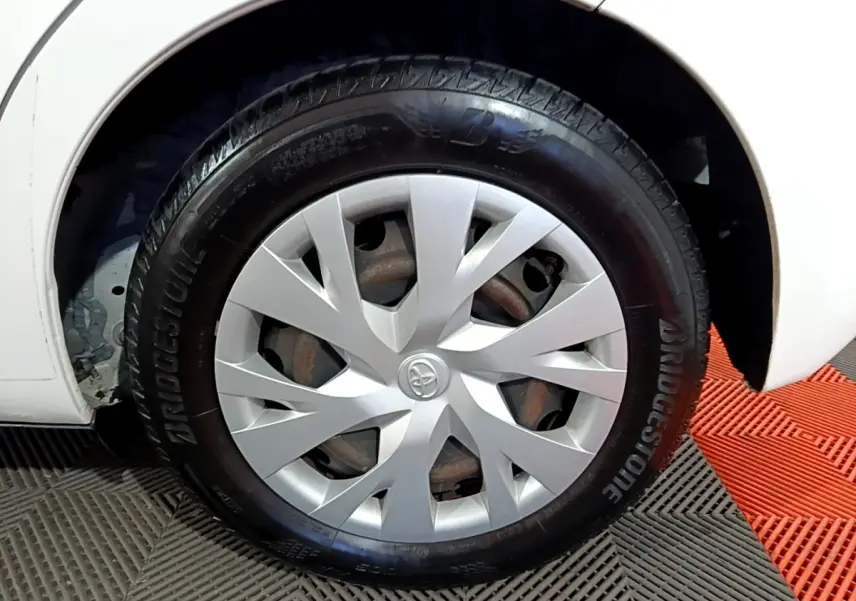 Gros plan sur la roue avant droite d'une Toyota Yaris blanche, avec enjoliveur argenté et pneu Bridgestone.