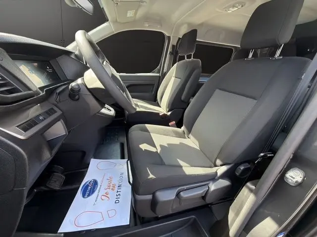 Vue intérieure côté conducteur du Citroën Jumpy gris titane, montrant les sièges avant en tissu bi-ton noir-gris et le tableau de bord.