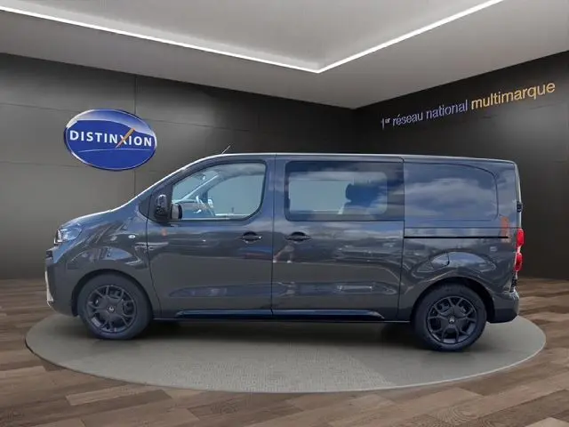 Vue latérale droite du Citroën Jumpy gris titane 2026 avec jantes noires et portes coulissantes en intérieur showroom.