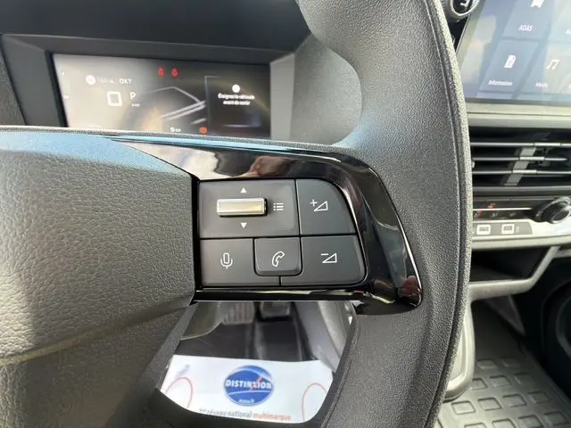 Gros plan sur les commandes au volant côté gauche du Citroën Jumpy gris titane, avec tableau de bord numérique en arrière-plan.