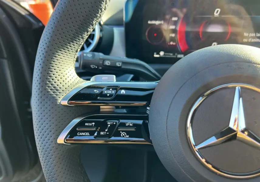 Gros plan sur le volant cuir perforé noir de la Mercedes Classe A 200D, avec commandes multifonctions et tableau de bord numérique.