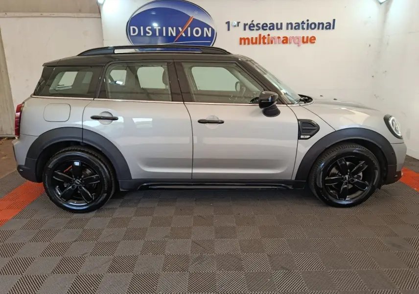 Vue de profil droit d'un MINI Countryman gris foncé avec toit noir et jantes noires brillantes dans un showroom.
