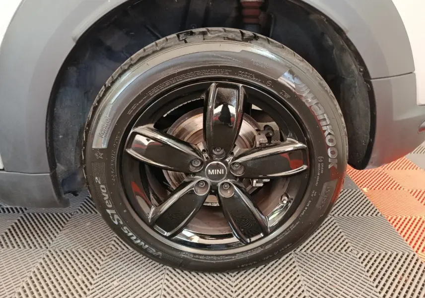 Gros plan sur la roue avant gauche d'une MINI Countryman gris foncé avec jante noire brillante à cinq branches.