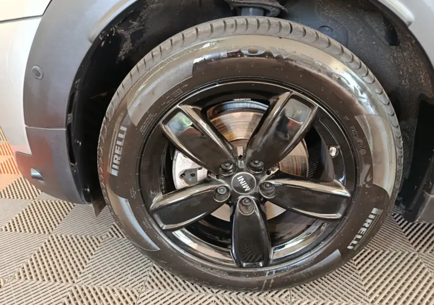 Gros plan sur la roue avant droite du MINI Countryman gris foncé, jante noire brillante à cinq branches.