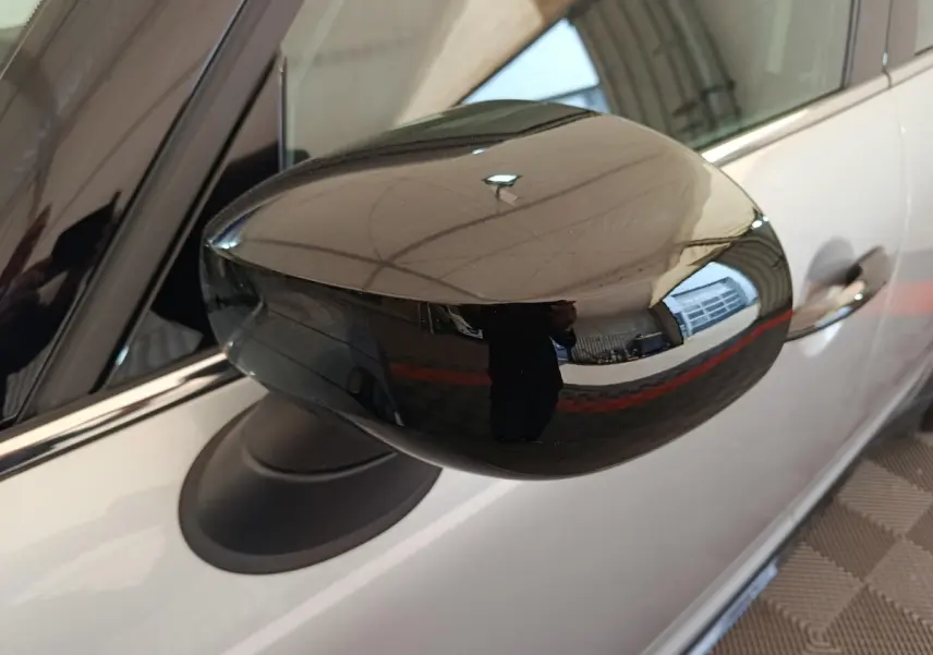 Gros plan sur le rétroviseur noir brillant côté gauche d'un MINI Countryman gris foncé, avec reflet de l'environnement intérieur.