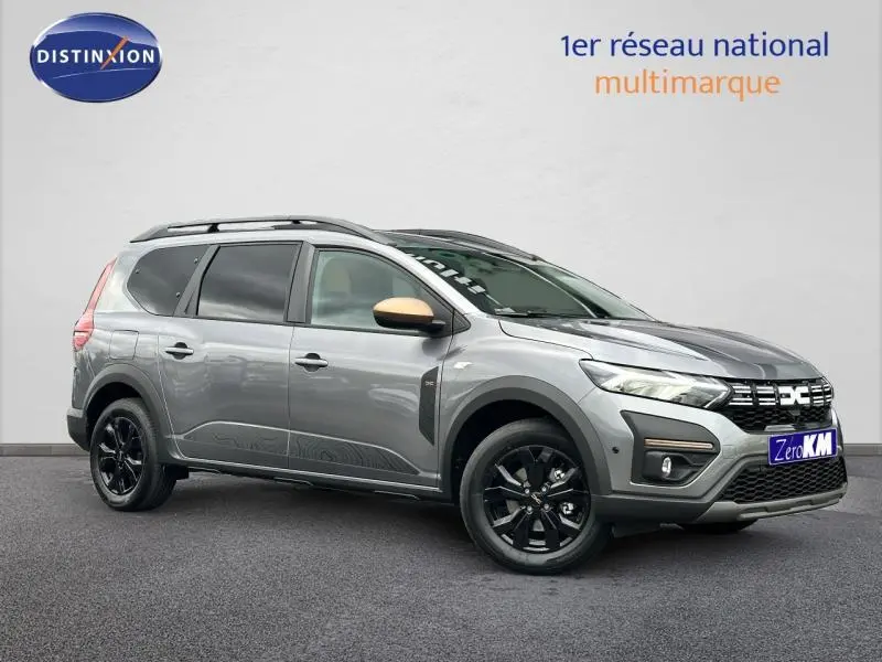 Vue 3/4 avant droit du Dacia Jogger gris schiste métallisé avec jantes noires et barres de toit visibles.