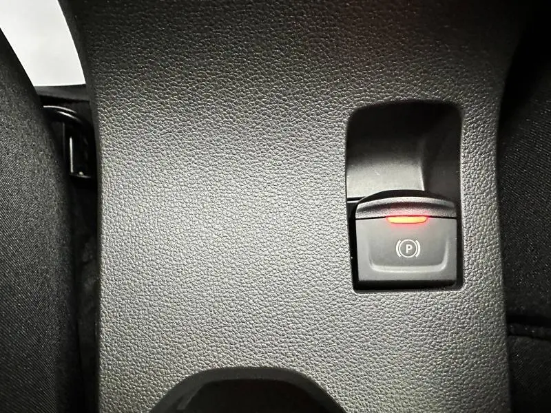 Gros plan sur le bouton de frein de stationnement électrique avec témoin rouge dans l'habitacle du Dacia Jogger gris Schiste.
