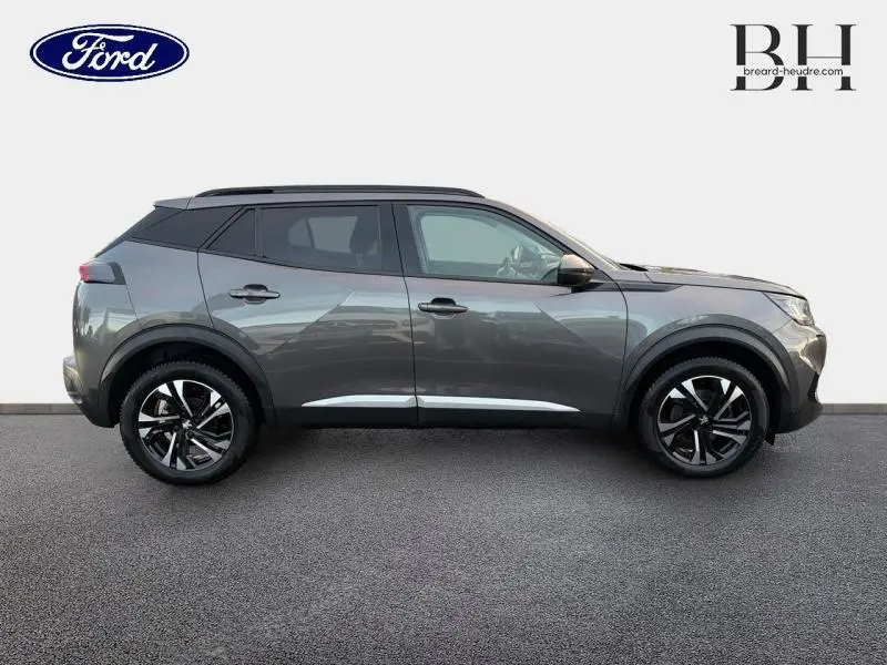 Profil droit d'un Peugeot 2008 gris Artense 2021 avec jantes alliage noires et barres de toit visibles.