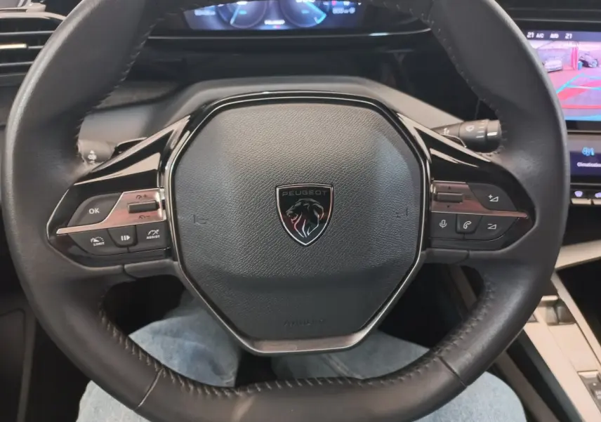 Vue rapprochée du volant cuir multifonctions noir de la Peugeot 308 PureTech 130, avec tableau de bord digital en arrière-plan.