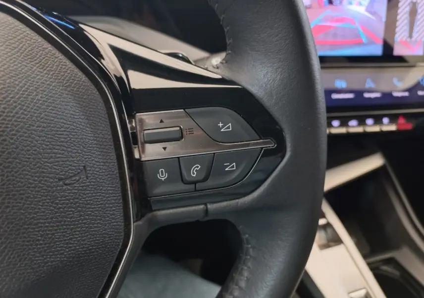 Gros plan sur le volant cuir multifonctions à gauche de la Peugeot 308 bleu, avec commandes audio et vocales visibles.