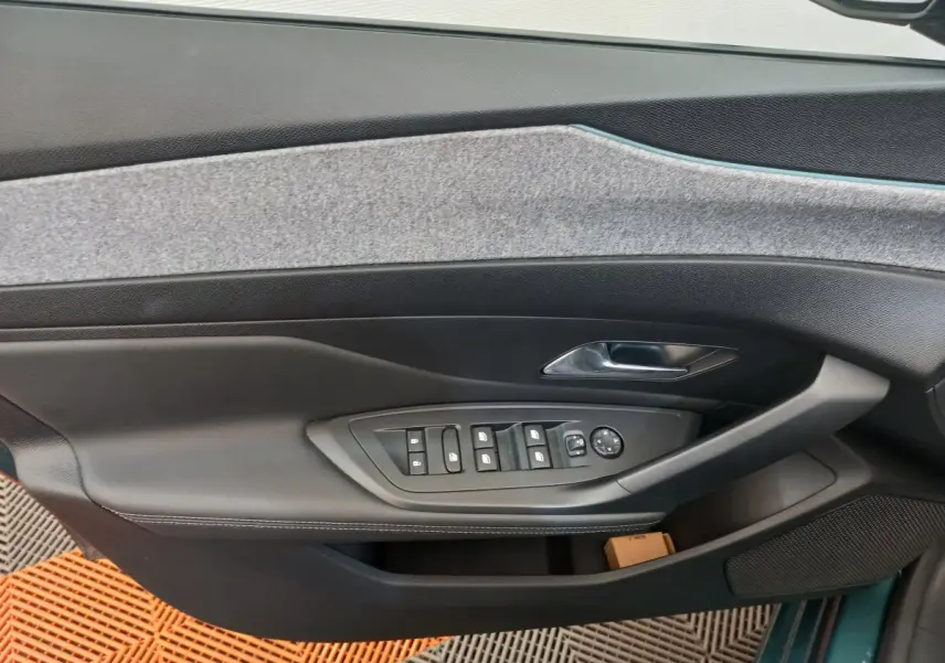 Vue intérieure côté gauche de la porte avant d'une Peugeot 308 bleu, avec commandes électriques des vitres et poignée chrome.