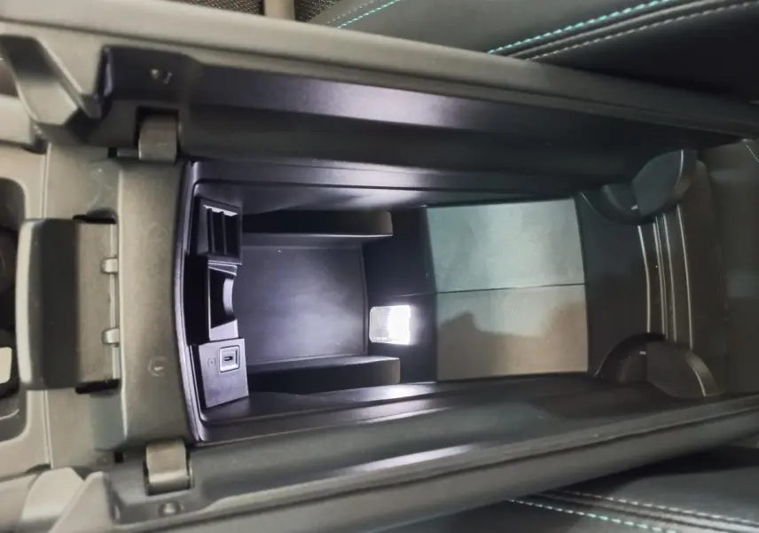 Vue en plongée de la console centrale ouverte de la Peugeot 308 bleu, montrant un espace de rangement avec port USB intégré.