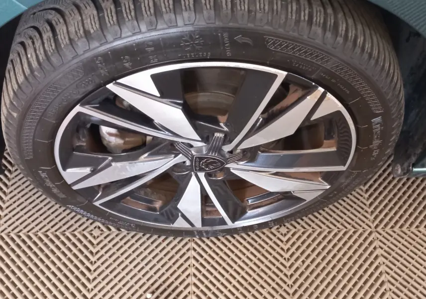 Gros plan sur la jante alliage bicolore noire et argentée d'une Peugeot 308 bleu 2022, vue de dessus.
