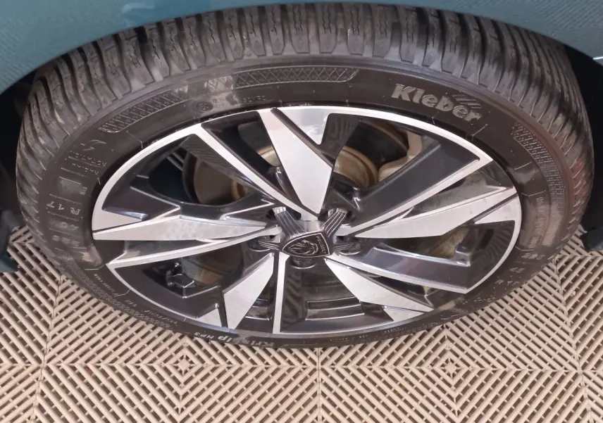 Gros plan sur la roue avant droite d’une Peugeot 308 bleu, jante alliage bicolore au design moderne.
