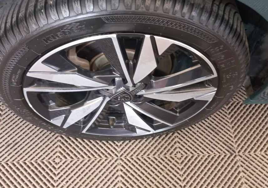Gros plan sur la roue avant droite de la Peugeot 308 bleu, avec jante alliage noire et argentée au design moderne.