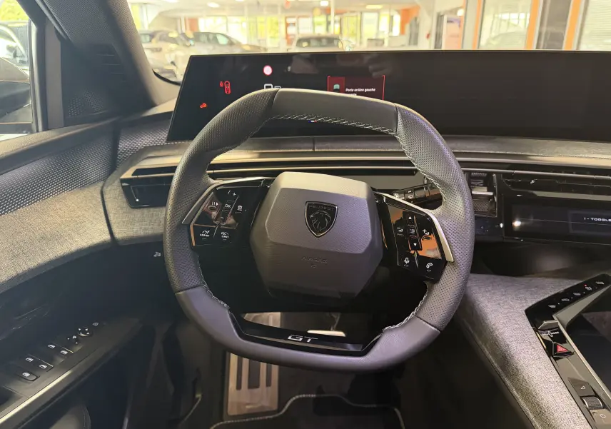 Vue intérieure centrée sur le volant GT du Peugeot 3008 Hybrid 145, avec tableau de bord numérique et sellerie tissu gris.