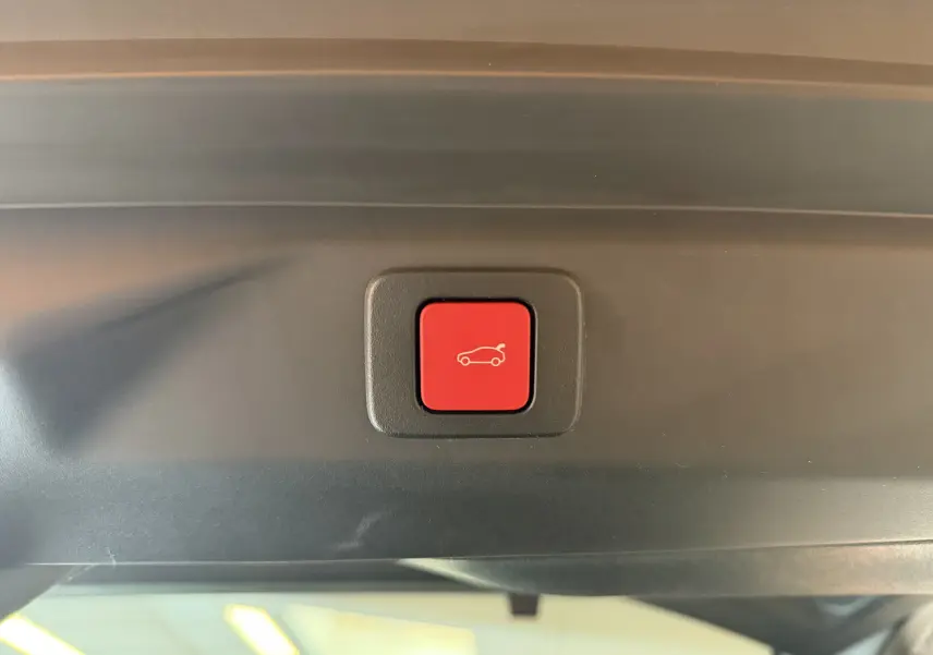 Bouton rouge d'ouverture électrique du hayon visible en gros plan à l'intérieur du Peugeot 3008 Hybrid 145 GT bleu obsession.