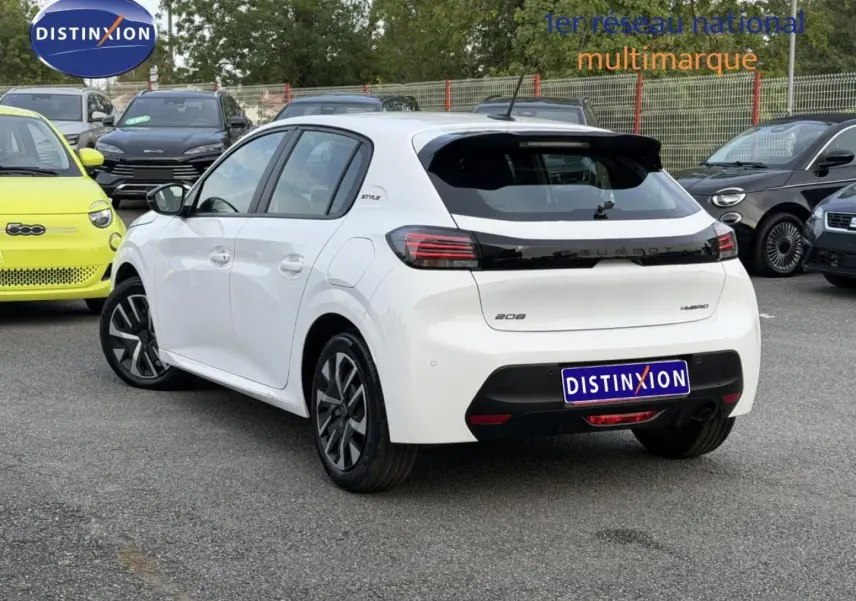 Vue 3/4 arrière droite d'une Peugeot 208 blanche Okénite avec détails noirs et jantes stylisées, stationnée en extérieur.