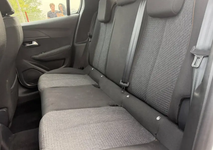 Vue intérieure côté droit sur la banquette arrière tissu gris foncé avec surpiqûres orange de la Peugeot 208 blanche.