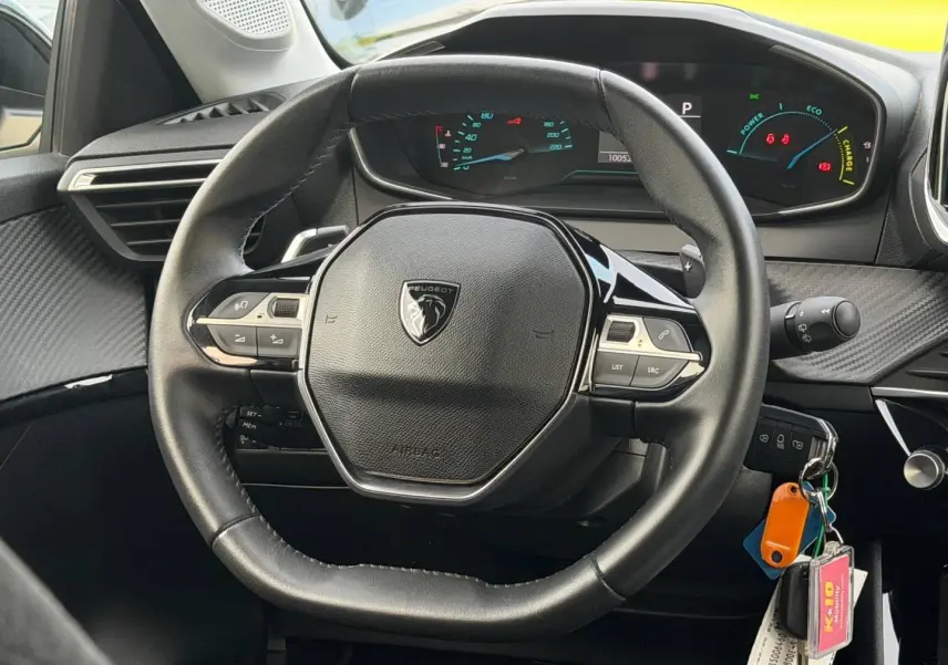 Vue intérieure centrée sur le volant noir de la Peugeot 208 1.2 Hybrid 110ch avec tableau de bord numérique allumé.