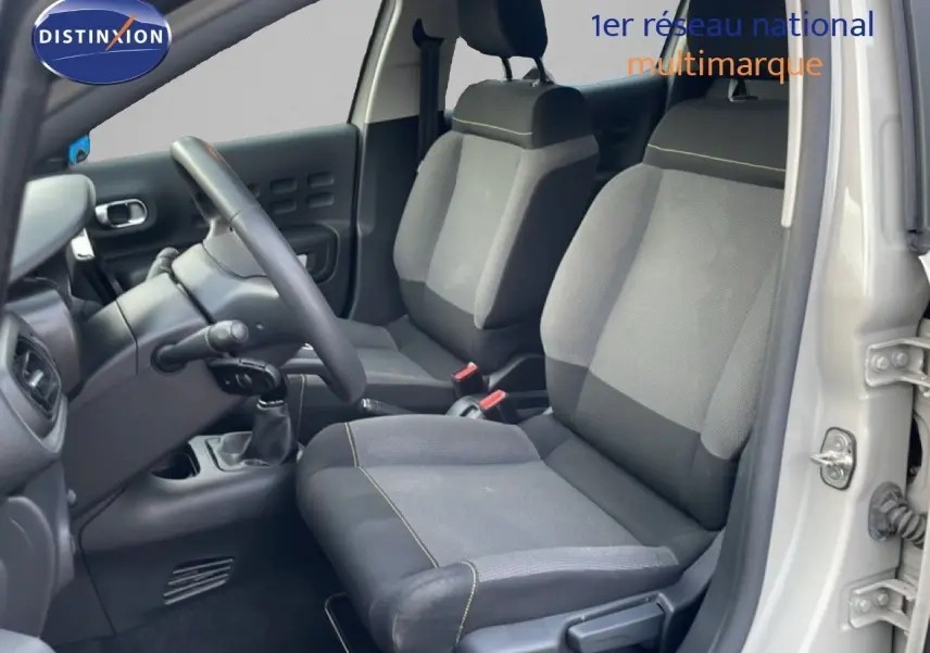 Vue intérieure côté conducteur de la Citroën C3 2022 sable métal, montrant les sièges en tissu gris et la boîte manuelle.