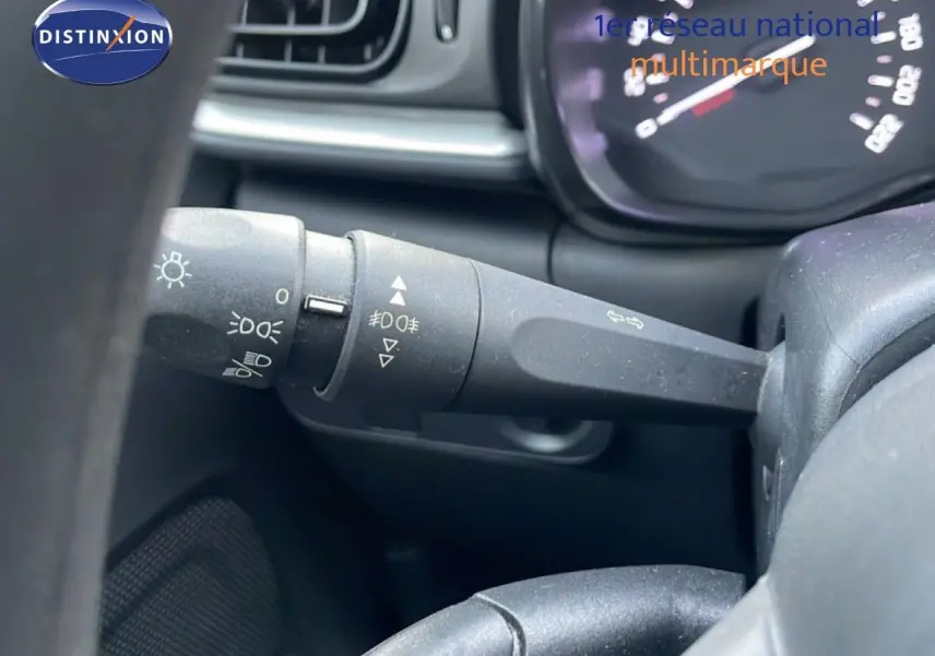 Gros plan sur la manette de commande des phares à gauche du volant dans l’habitacle d’une Citroën C3 sable métal.