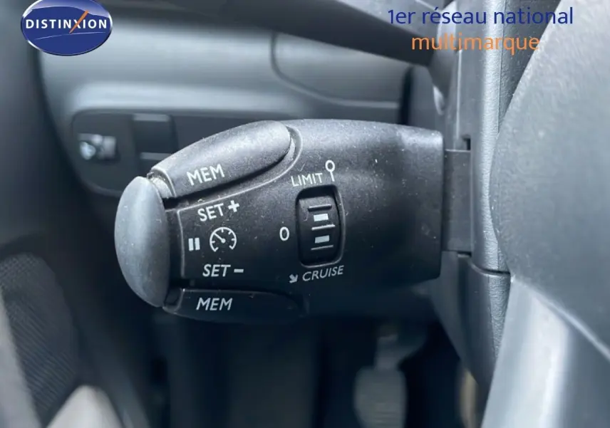 Gros plan sur la commande de régulateur de vitesse noire à gauche du volant d'une Citroën C3 sable métal.