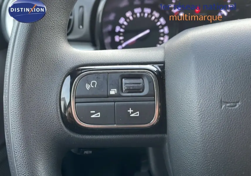 Gros plan sur les commandes au volant d'une Citroën C3 2022 sable métal, avec tableau de bord flou en arrière-plan.