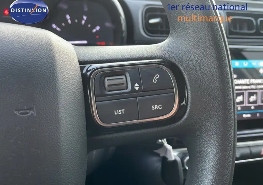 Gros plan sur les commandes au volant noir de la Citroën C3 sable métal, avec tableau de bord et écran tactile en arrière-plan.