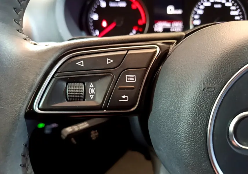 Gros plan sur le côté gauche du volant cuir noir de l'Audi A3 30 TDI 2019 avec commandes multifonctions.