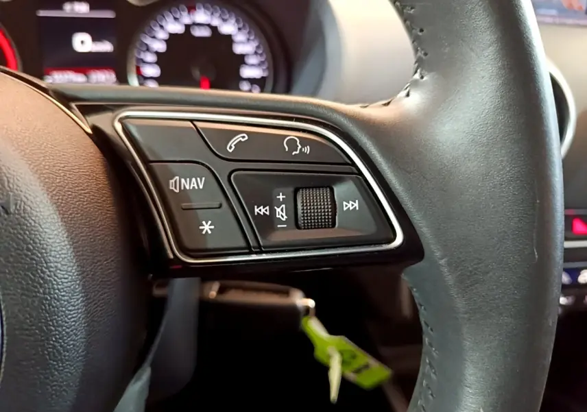 Gros plan sur le volant cuir noir d'une Audi A3 2019, avec commandes multifonctions et tableau de bord flou en arrière-plan.