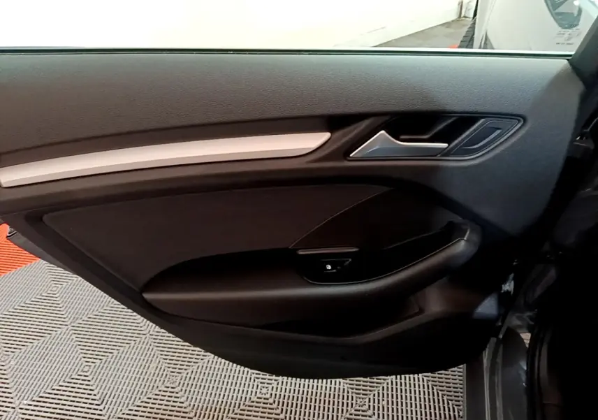 Vue intérieure de la porte avant gauche d'une Audi A3 gris foncé, avec poignée et commande de verrouillage intégrées.