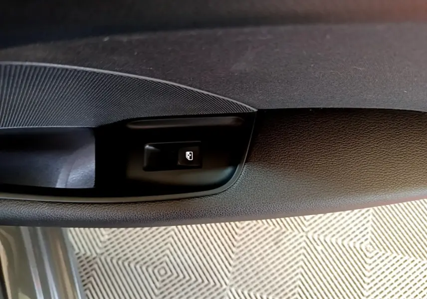 Détail du bouton d'ouverture de coffre sur la porte intérieure côté conducteur d'une Audi A3 gris foncé.