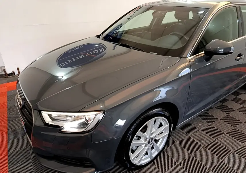 Vue 3/4 avant droit d'une Audi A3 gris foncé brillante avec jantes alliage et phares LED allumés.