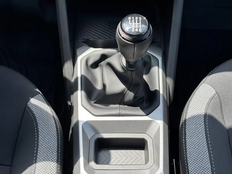 Vue plongeante sur le levier de vitesse manuel noir et gris du Dacia Bigster blanc, entouré des sièges avant en tissu.