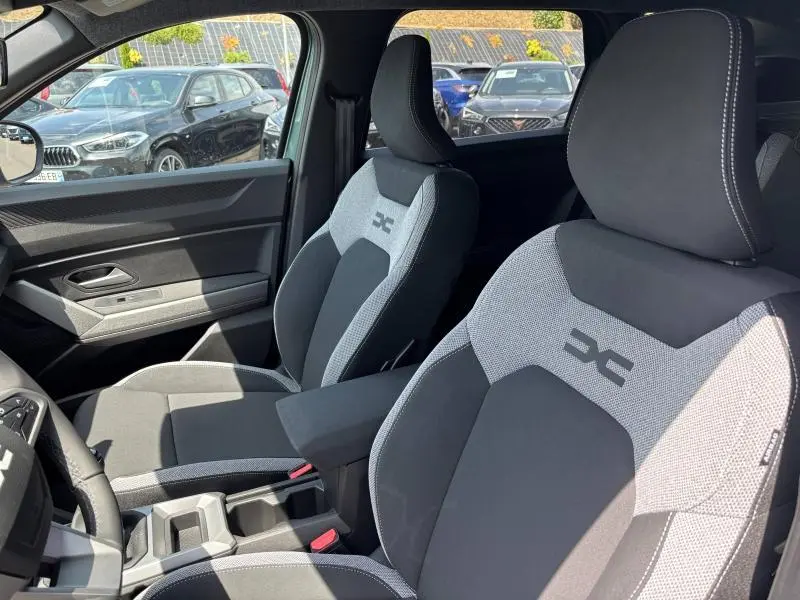 Vue intérieure côté gauche des sièges avant gris clair et noir du Dacia Bigster 2025 avec accoudoir central et logo DC brodé.