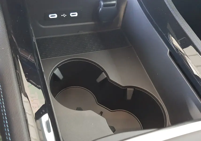 Gros plan sur la console centrale noire du Renault Austral E-Tech avec porte-gobelets et ports USB visibles.