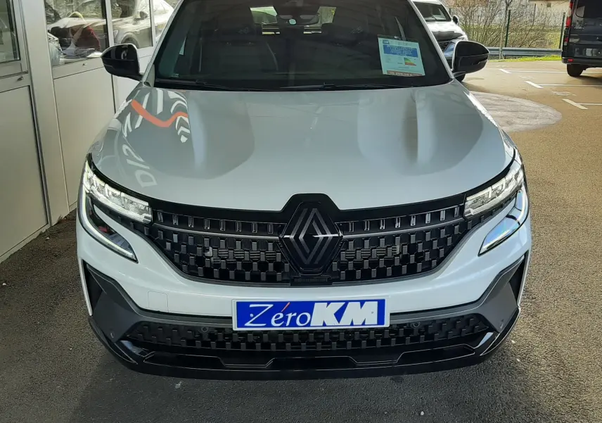 Vue avant d'un Renault Austral blanc nacré avec toit noir, calandre noire et plaque "Zéro KM" visible.