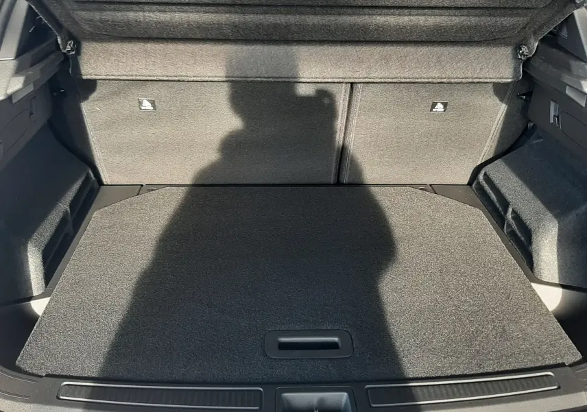 Coffre ouvert vu de l'arrière du Renault Austral blanc nacré, montrant un espace de chargement plat et habillé de moquette grise.