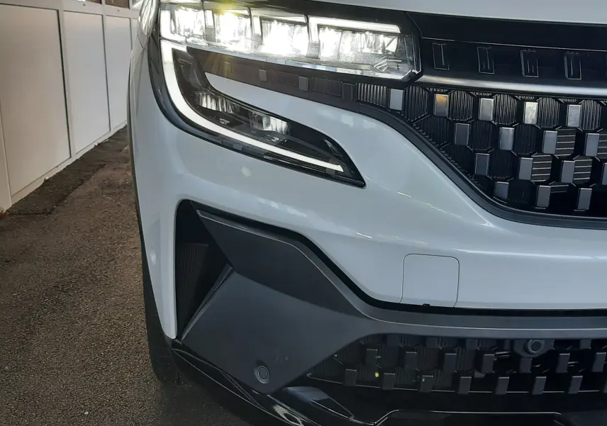 Gros plan sur l’avant gauche du Renault Austral blanc nacré avec toit noir, mettant en valeur les phares LED et la calandre noire.