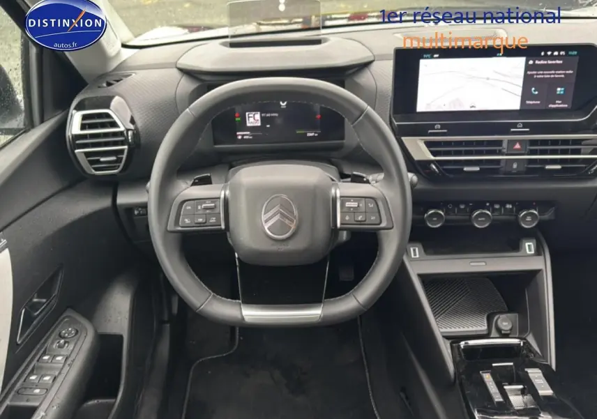 Vue intérieure frontale du poste de conduite noir de la Citroën C4 hybride 2025 avec écran tactile et volant multifonction.
