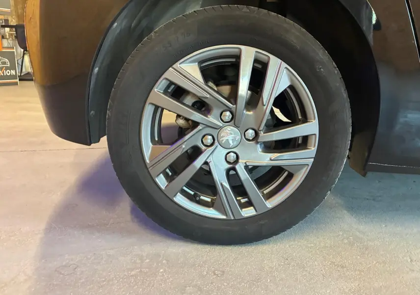 Gros plan sur la roue avant gauche d'une Peugeot 208 noire, mettant en valeur la jante alliage au design moderne.