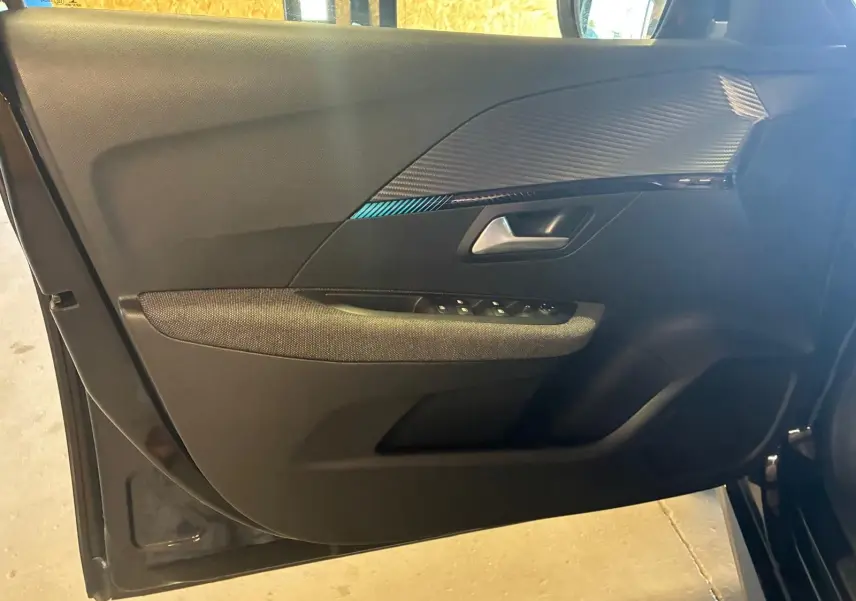 Vue intérieure de la porte côté gauche d'une Peugeot 208 noire, avec garniture tissu et inserts décoratifs noirs.