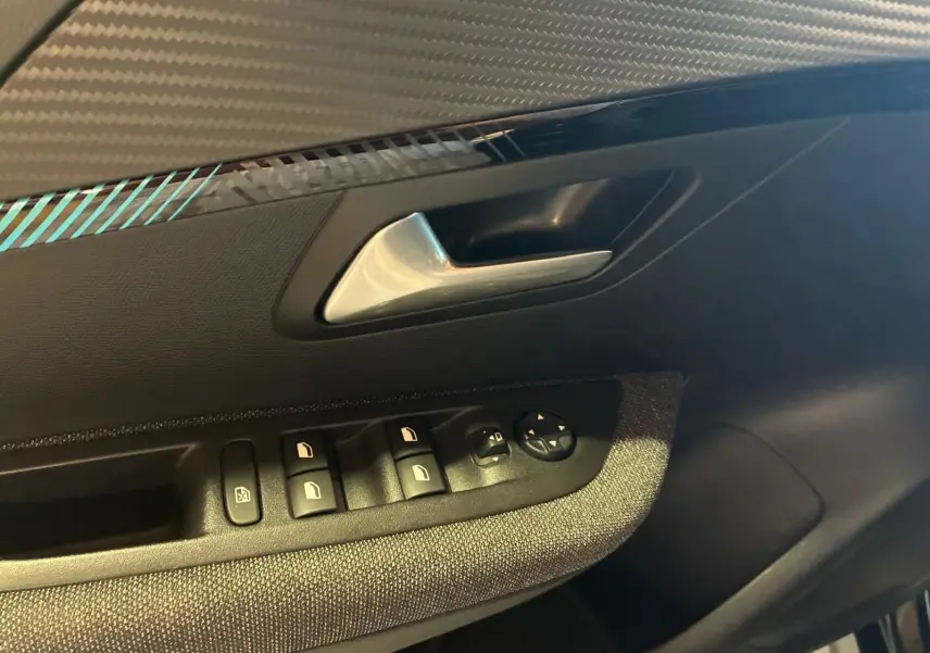 Gros plan sur la poignée intérieure côté gauche de la porte d’une Peugeot 208 noire avec commandes des vitres et rétroviseurs.