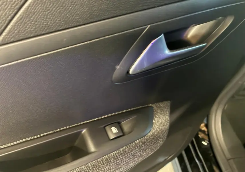 Détail de la porte intérieure côté gauche de la Peugeot 208 noire, avec poignée argentée et commande de vitre électrique.