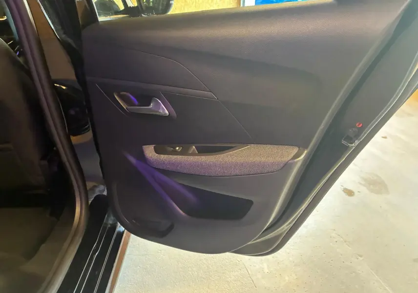 Porte arrière gauche ouverte d’une Peugeot 208 noire 2021, intérieur tissu noir avec poignée argentée.
