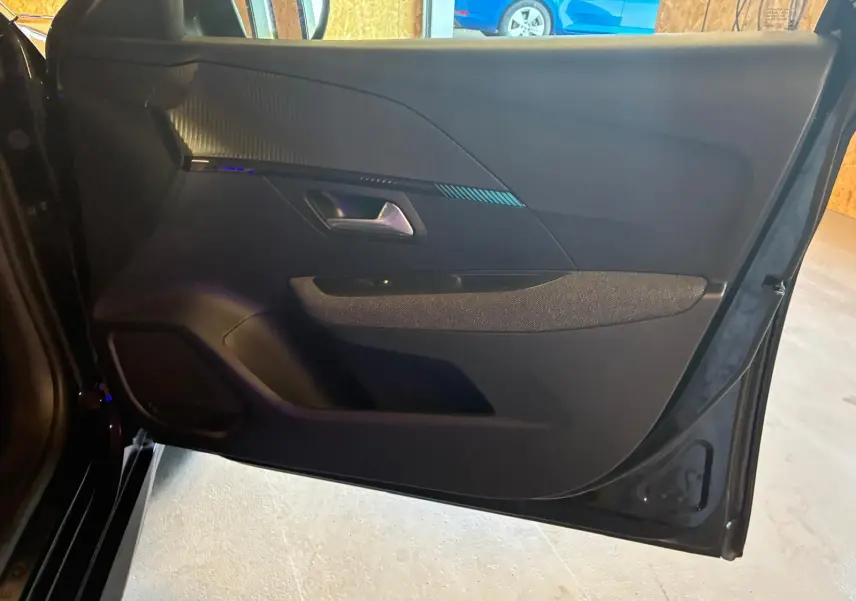 Vue intérieure de la porte avant gauche noire d'une Peugeot 208 1.5 BlueHDi 100 Style avec garniture tissu et plastique.