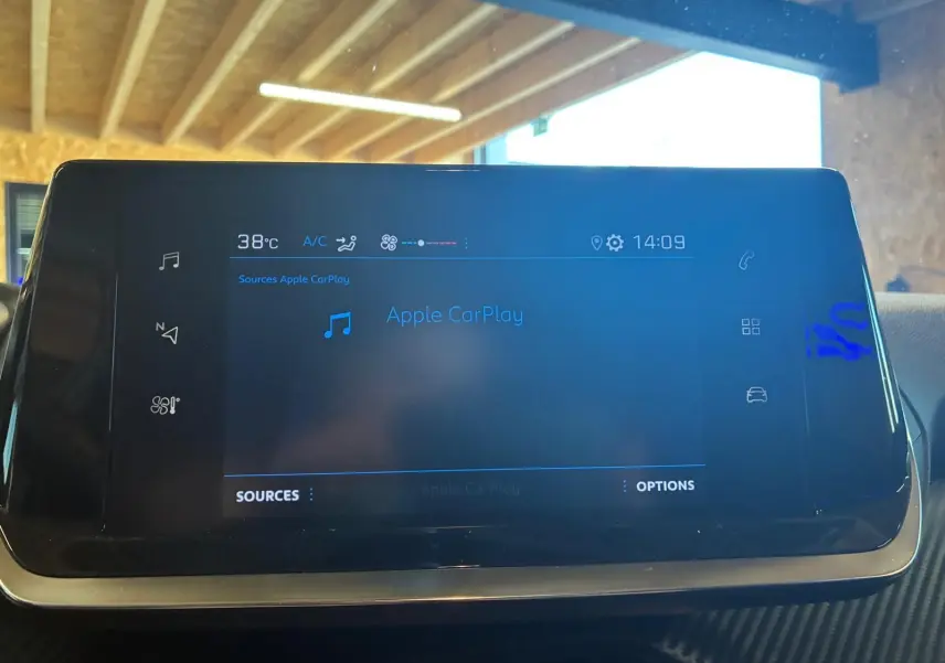 Écran tactile central du tableau de bord de la Peugeot 208 noir, affichant Apple CarPlay et la température à 38°C.